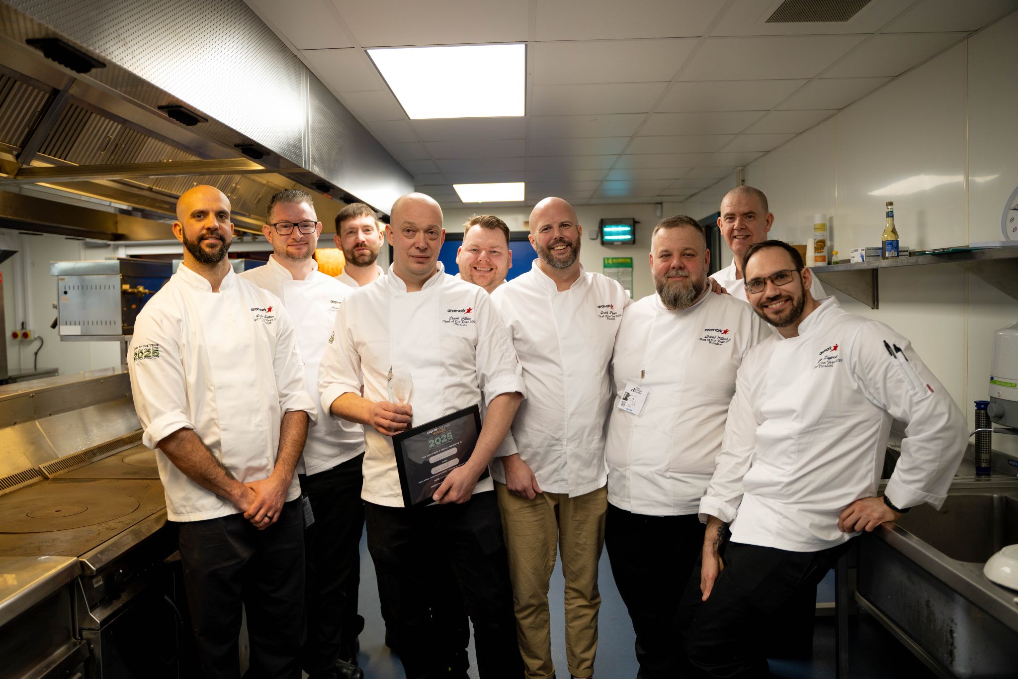 chefs posing in kitchen with Stuart holding award